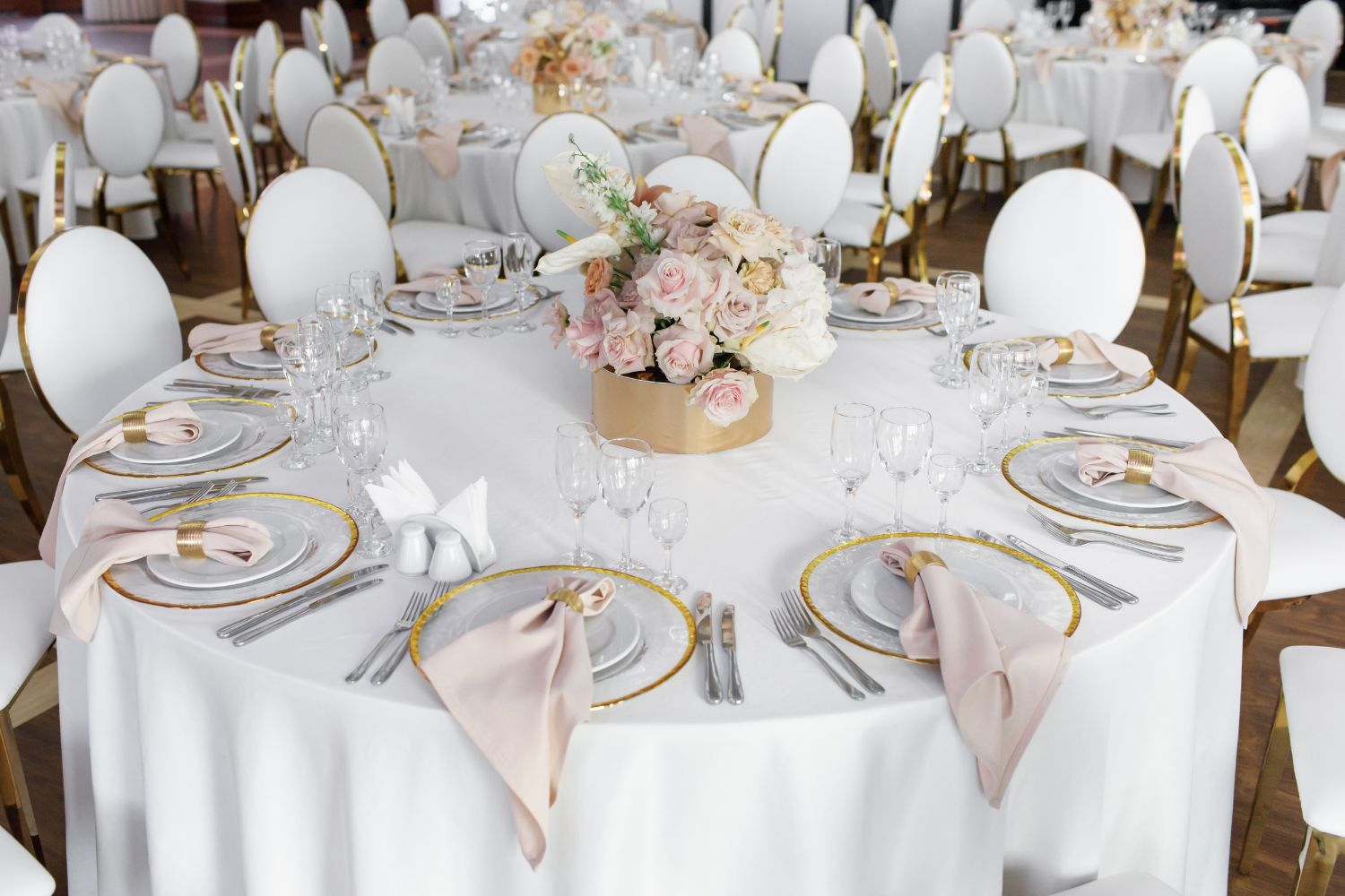 Nowoczesna sala weselna z okrągłymi stołami, pastelowymi dekoracjami i eleganckimi krzesłami - przykład uniwersalnego lokalu na wesele w stylu klasycznym.